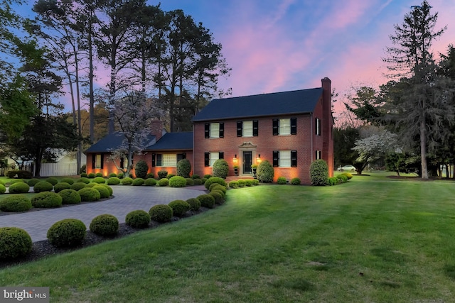 colonial house featuring a chimney, a yard, and brick siding