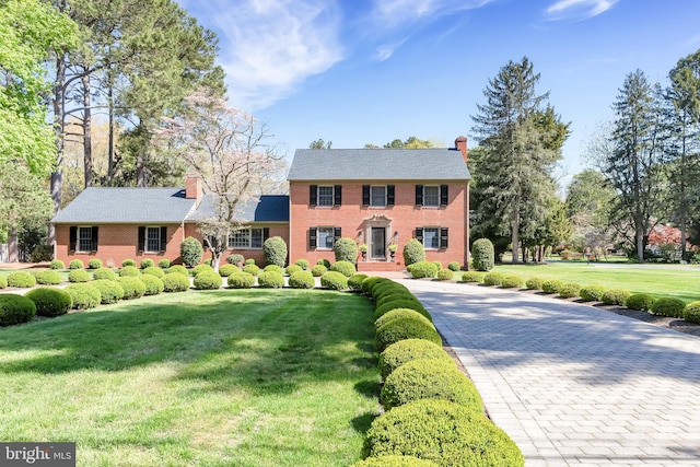 colonial house with a chimney, a front yard, and brick siding