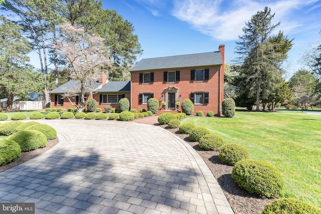 colonial-style house with curved driveway, brick siding, a front lawn, and a chimney