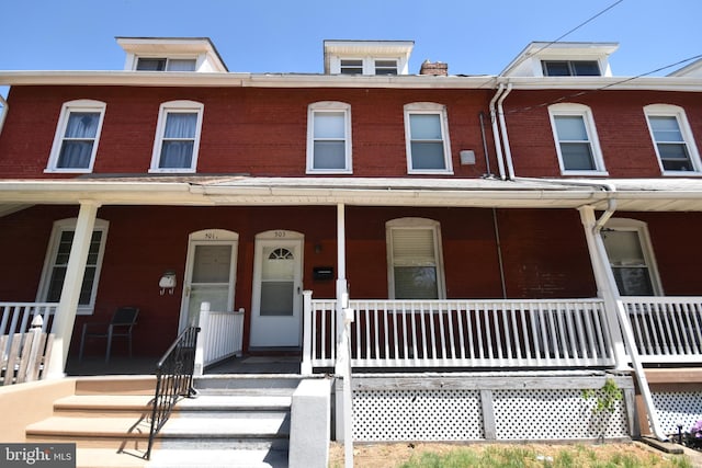 townhome / multi-family property featuring covered porch and brick siding