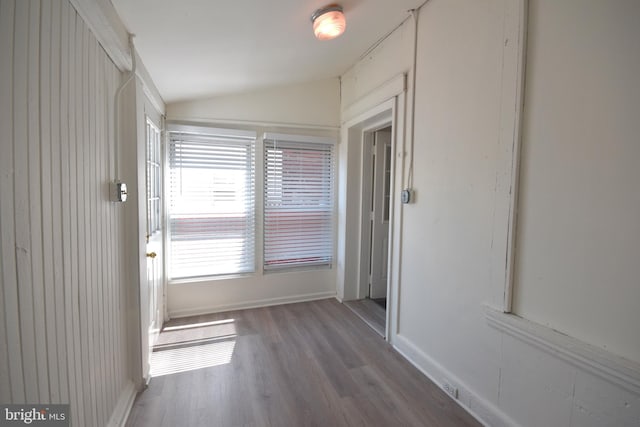 hallway with baseboards, vaulted ceiling, and wood finished floors