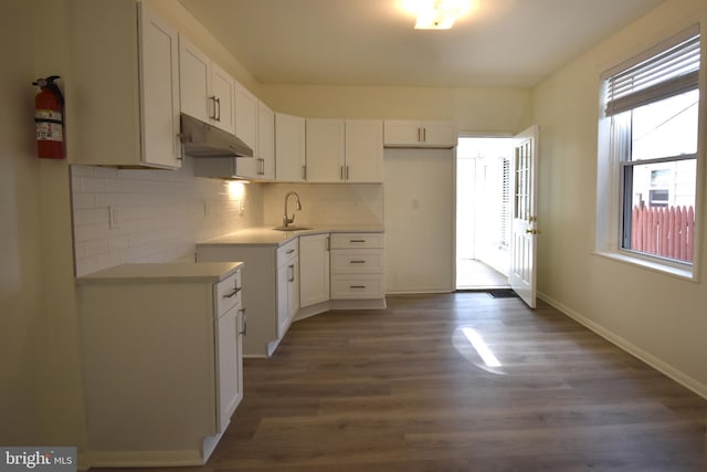 kitchen featuring white cabinets, backsplash, baseboards, dark wood-type flooring, and under cabinet range hood