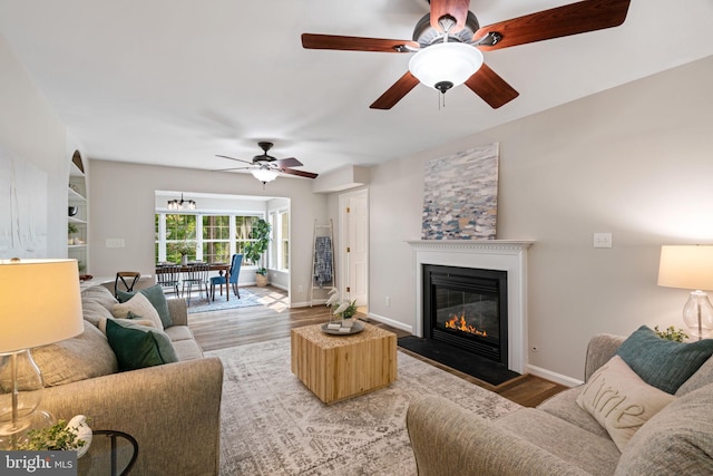 living area with a ceiling fan, baseboards, a fireplace with flush hearth, and wood finished floors