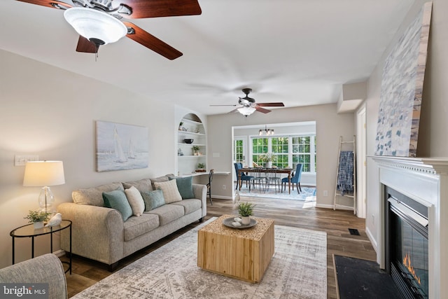 living area featuring a ceiling fan, baseboards, a fireplace with flush hearth, and wood finished floors