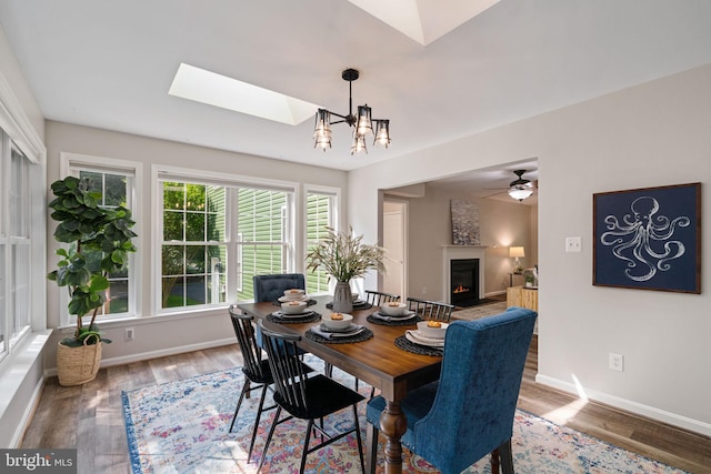 dining room featuring baseboards, wood finished floors, a skylight, and a warm lit fireplace