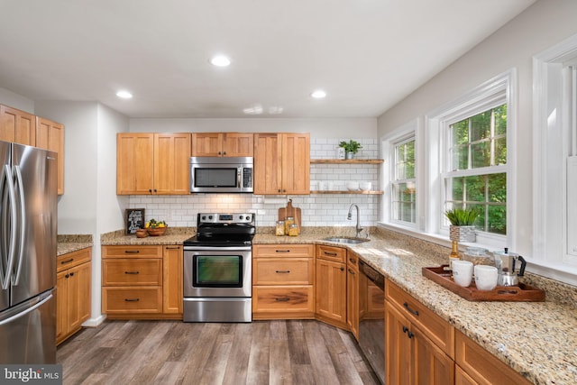 kitchen with a sink, stainless steel appliances, wood finished floors, open shelves, and backsplash