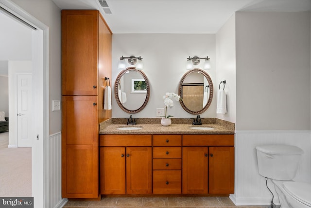 full bathroom with toilet, a wainscoted wall, visible vents, and a sink