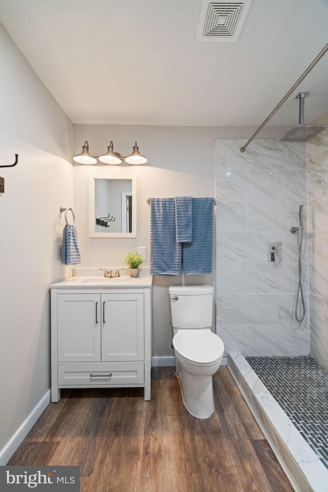 bathroom featuring toilet, wood finished floors, vanity, visible vents, and tiled shower