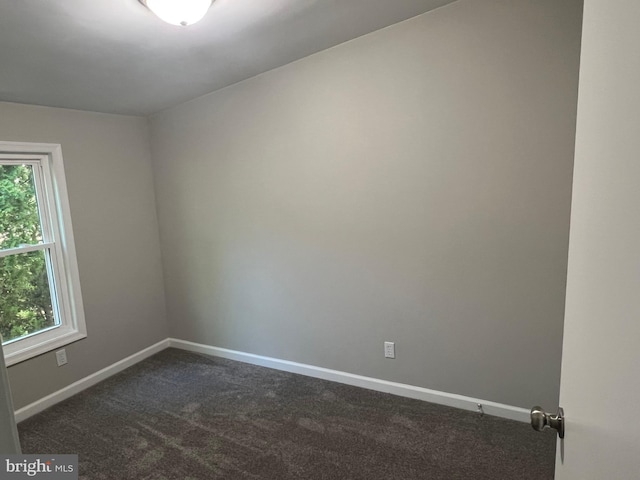 spare room with dark colored carpet, baseboards, and a healthy amount of sunlight