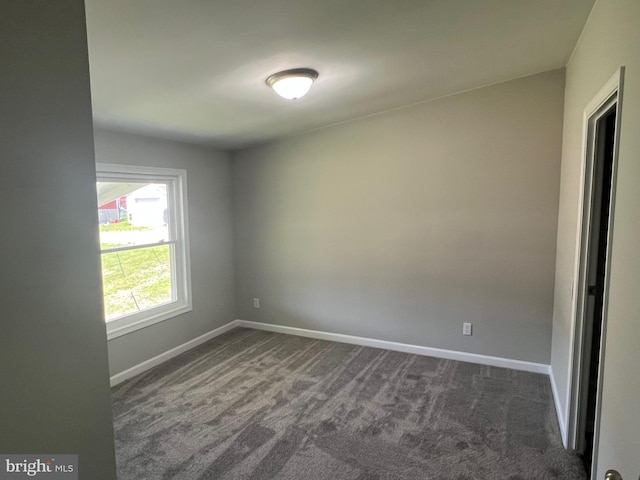 unfurnished room with baseboards and dark colored carpet