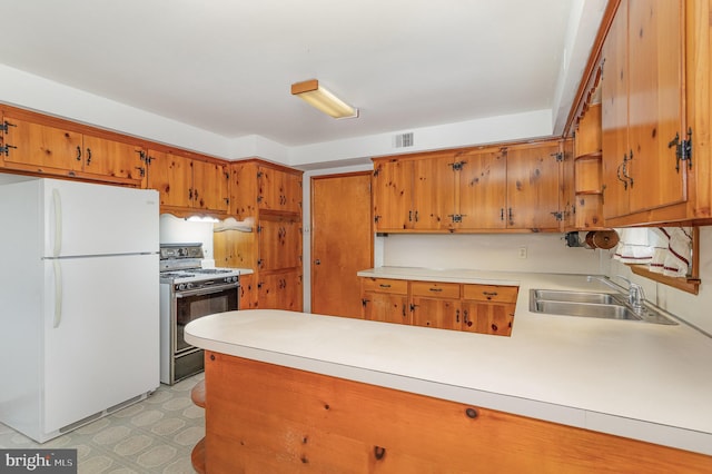 kitchen featuring brown cabinets, gas stove, light countertops, freestanding refrigerator, and visible vents
