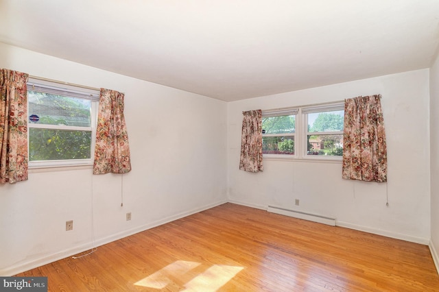 empty room featuring light wood-style floors, a baseboard radiator, and baseboards