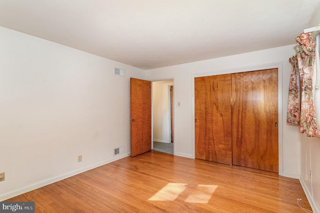 unfurnished bedroom featuring baseboards, a closet, light wood finished floors, and visible vents
