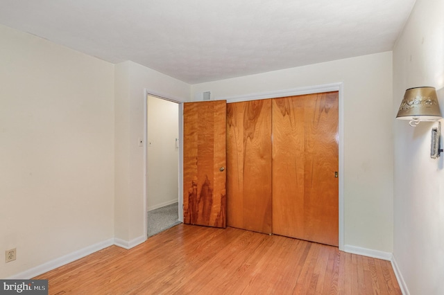 unfurnished bedroom with baseboards, a closet, wood finished floors, and visible vents
