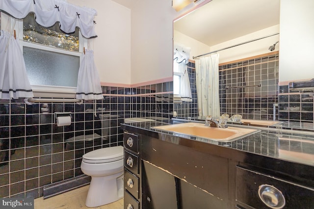 full bath featuring tile walls, a wainscoted wall, vanity, and toilet
