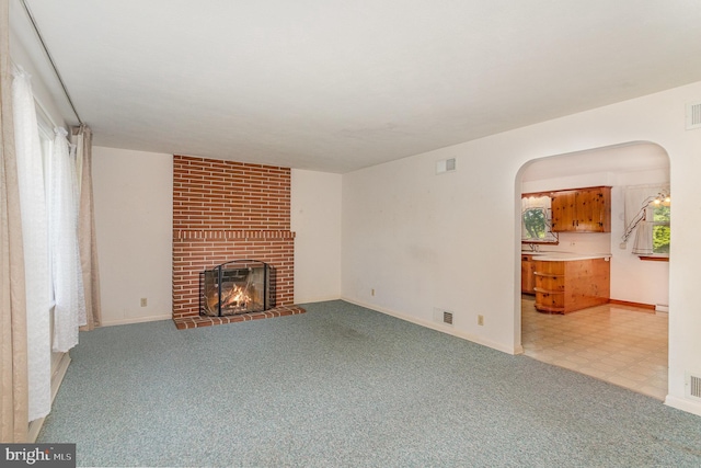 unfurnished living room featuring visible vents, arched walkways, a brick fireplace, and light colored carpet