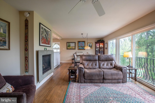 living room with baseboards, ceiling fan, wood finished floors, and a tile fireplace