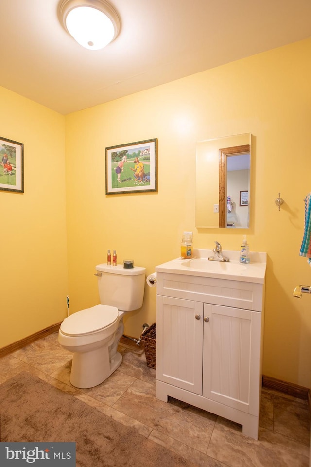 half bathroom featuring toilet, baseboards, and vanity