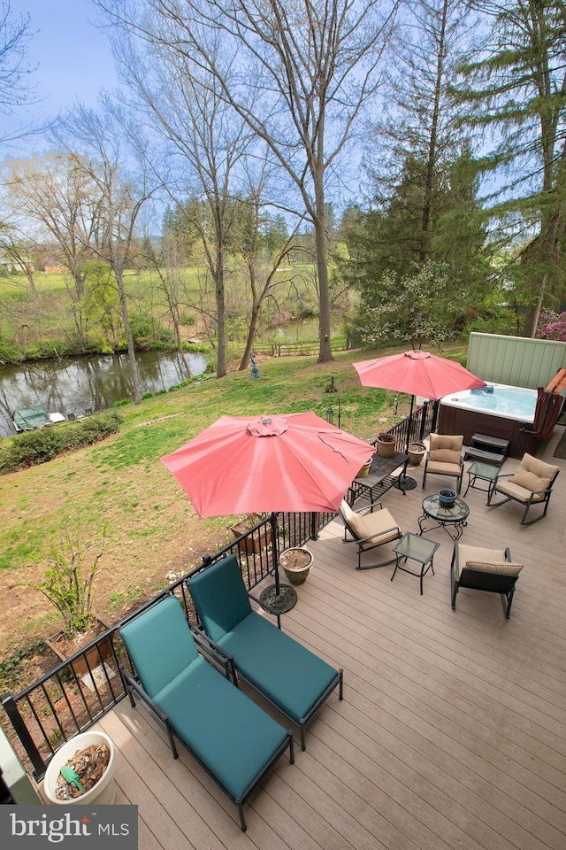 wooden deck with a yard, a water view, and a hot tub
