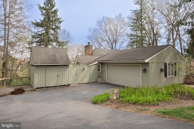 exterior space featuring a shingled roof, an attached garage, aphalt driveway, a storage shed, and a chimney