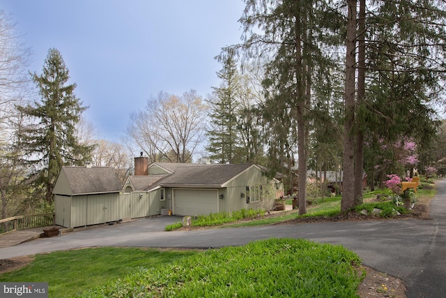 view of side of home with a chimney, an attached garage, and driveway