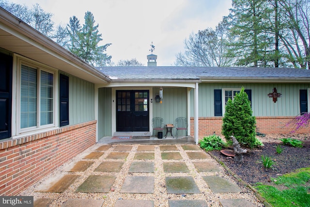 property entrance featuring board and batten siding, a chimney, a porch, and brick siding
