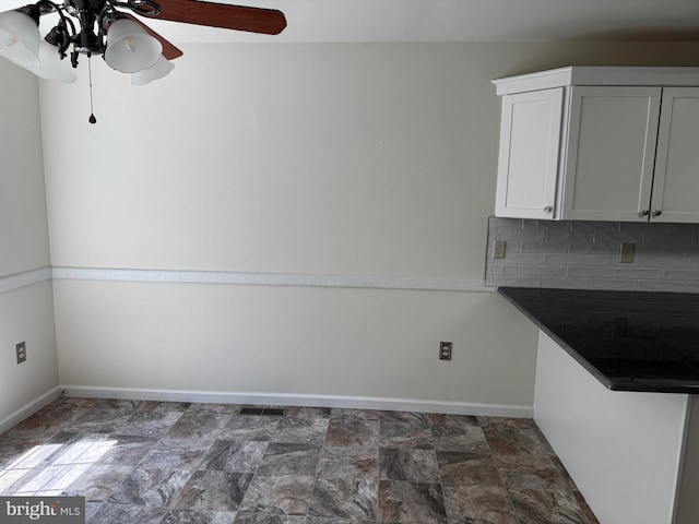 unfurnished dining area with baseboards, a ceiling fan, stone finish flooring, and visible vents