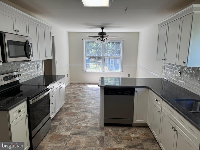 kitchen featuring a peninsula, ceiling fan, tasteful backsplash, stone finish flooring, and appliances with stainless steel finishes