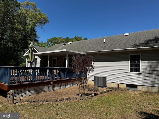 rear view of property with a shingled roof, central air condition unit, a yard, and a deck