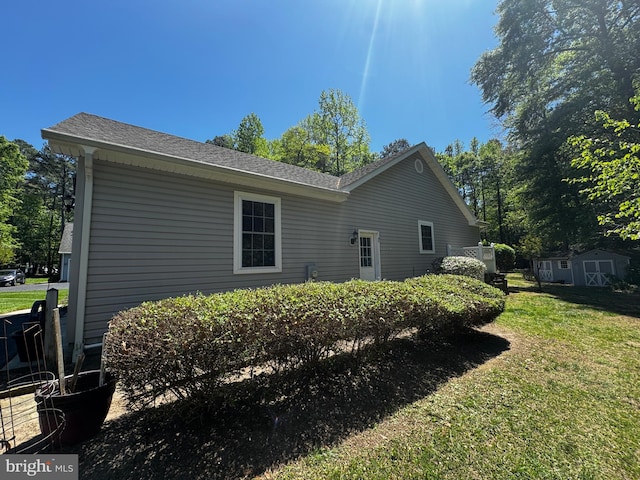 rear view of house featuring a lawn, an outbuilding, roof with shingles, and a storage unit