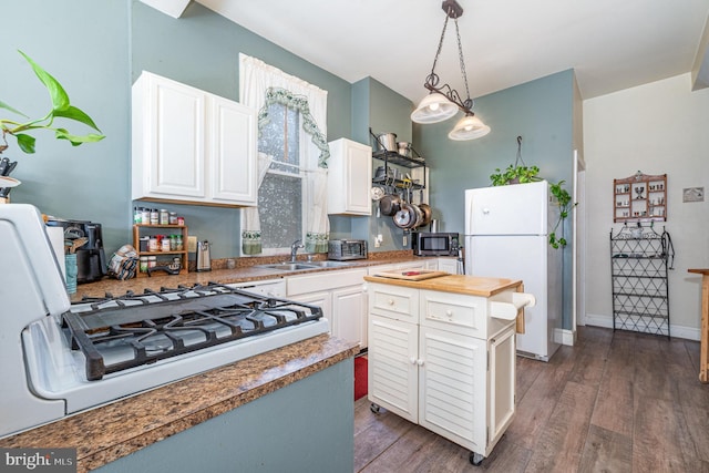 kitchen with a sink, stove, freestanding refrigerator, white cabinetry, and stainless steel microwave