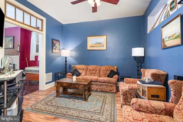 living area featuring a ceiling fan, baseboards, visible vents, and wood finished floors