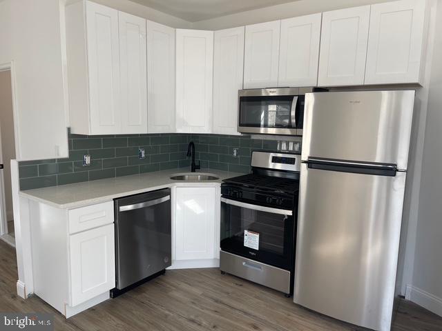 kitchen featuring white cabinetry, a sink, stainless steel appliances, light countertops, and wood finished floors
