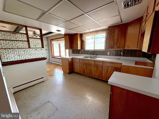 kitchen featuring baseboard heating, brown cabinets, a sink, light countertops, and a baseboard heating unit