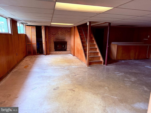 basement featuring a drop ceiling, wooden walls, and a fireplace