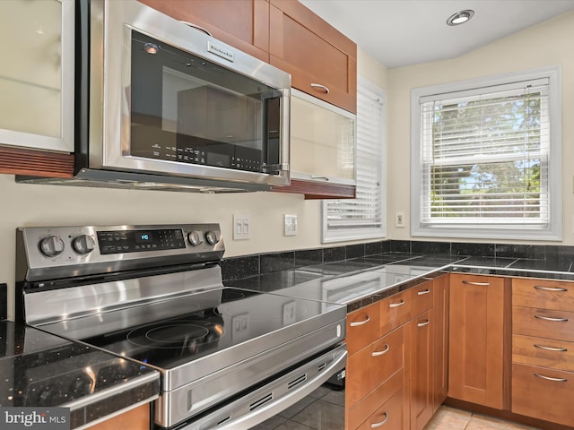 kitchen with brown cabinetry, light tile patterned floors, and stainless steel appliances