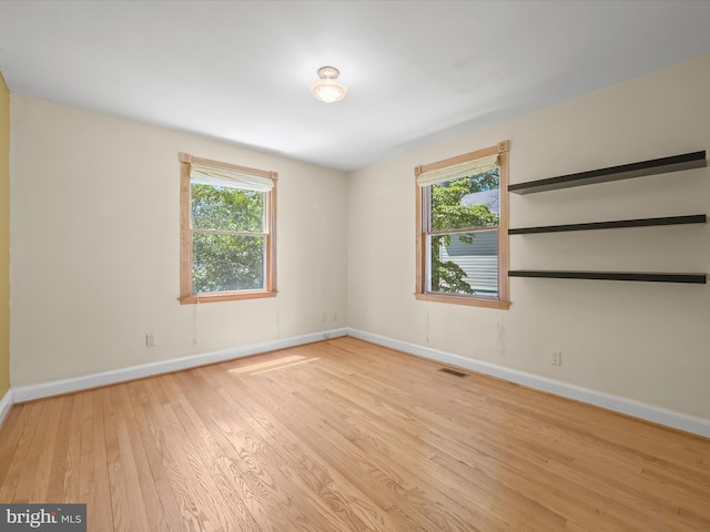 unfurnished room featuring baseboards, a wealth of natural light, wood finished floors, and visible vents