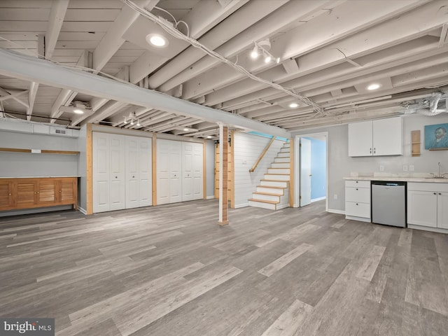 finished below grade area with a sink, light wood-style flooring, stairs, baseboards, and indoor bar