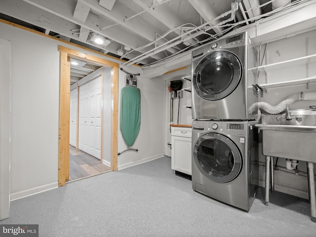 washroom with a sink, baseboards, stacked washer and clothes dryer, and cabinet space