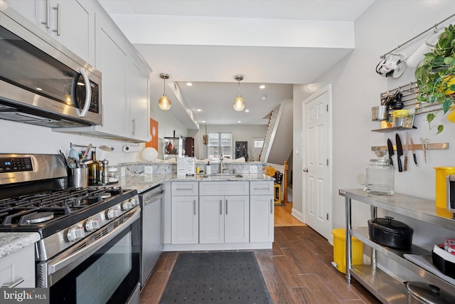 kitchen featuring light stone counters, stainless steel appliances, a sink, dark wood-style floors, and a peninsula