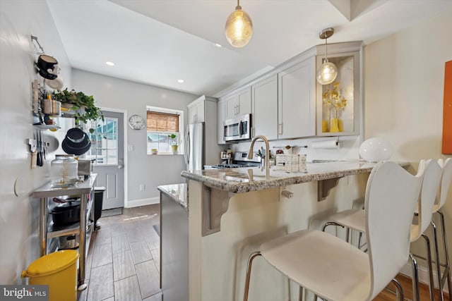 kitchen featuring light stone counters, pendant lighting, stainless steel appliances, a kitchen bar, and a peninsula