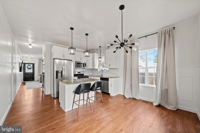 kitchen with light wood finished floors, a kitchen breakfast bar, a center island, stainless steel appliances, and white cabinetry