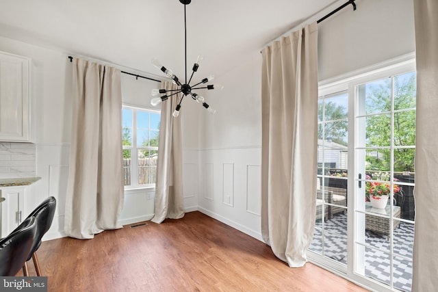 unfurnished dining area with visible vents, a decorative wall, light wood-style floors, a wainscoted wall, and a notable chandelier