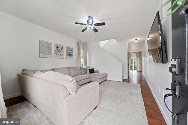 living room with baseboards, a ceiling fan, and dark wood-style floors