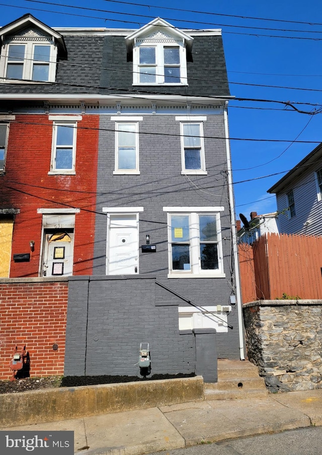 view of front facade featuring brick siding, fence, entry steps, and a shingled roof
