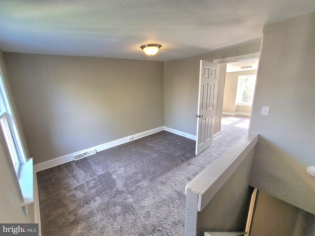 unfurnished room featuring baseboards, visible vents, dark carpet, and a textured ceiling