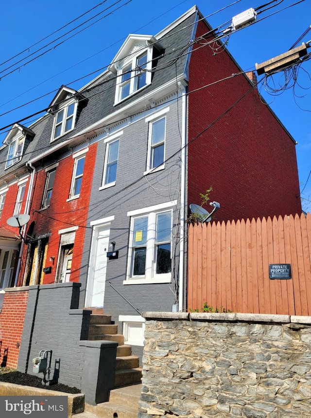 view of front facade with fence, entry steps, a shingled roof, and brick siding