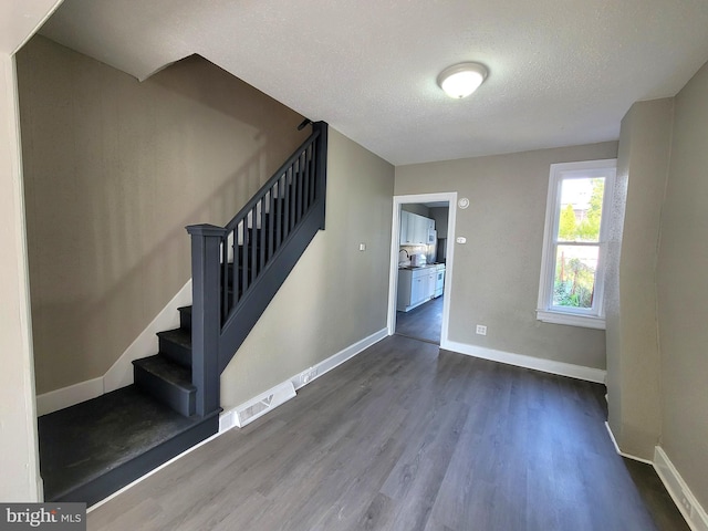 stairs with a textured ceiling, wood finished floors, visible vents, and baseboards