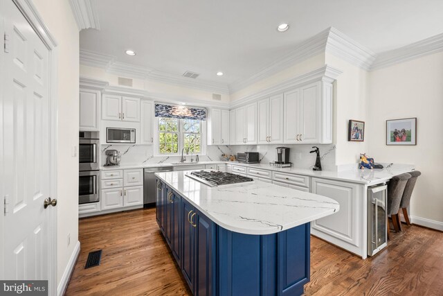 kitchen with appliances with stainless steel finishes, white cabinets, beverage cooler, wood finished floors, and a center island