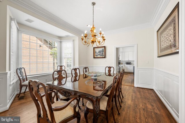 dining space featuring a chandelier, wainscoting, dark wood finished floors, crown molding, and a decorative wall